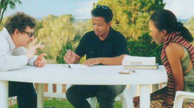 Trois personnes en discussion autour d’une table de jardin blanche avec des notes