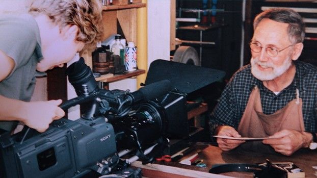 Camerawoman filming a wood engraver at his workbench