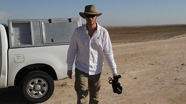Man with a hat and camera next to an off-road vehicle in the desert