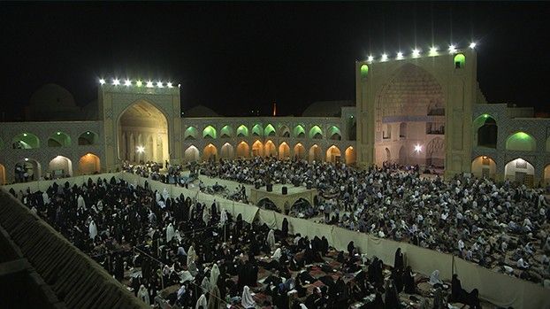 A large crowd at night prayer in the illuminated mosque courtyard