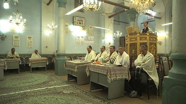 Men in prayer shawls in a synagogue with chandeliers