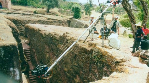 Caméra au bout d’un long bras de grue au-dessus d’une tranchée taillée dans la roche, l’équipe de tournage en haut