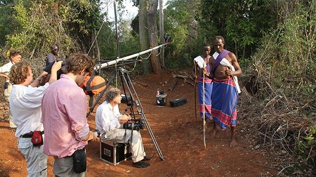 Film crew with a camera crane in the forest, two Mijikenda men in traditional dress