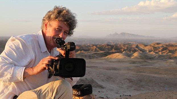 Rüdiger Lorenz with a video camera in front of a hilly landscape