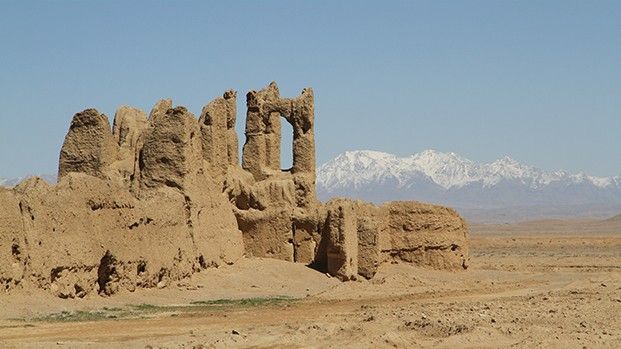 Mud-brick ruin of a caravanserai on the steppe, snow-capped mountains behind