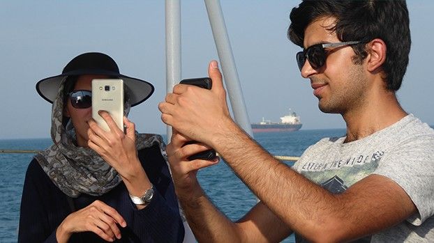 A young woman and a young man taking photos with smartphones on the deck of a ferry
