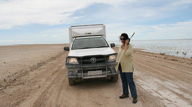Woman with a satellite phone next to an off-road vehicle in the Etosha Pan
